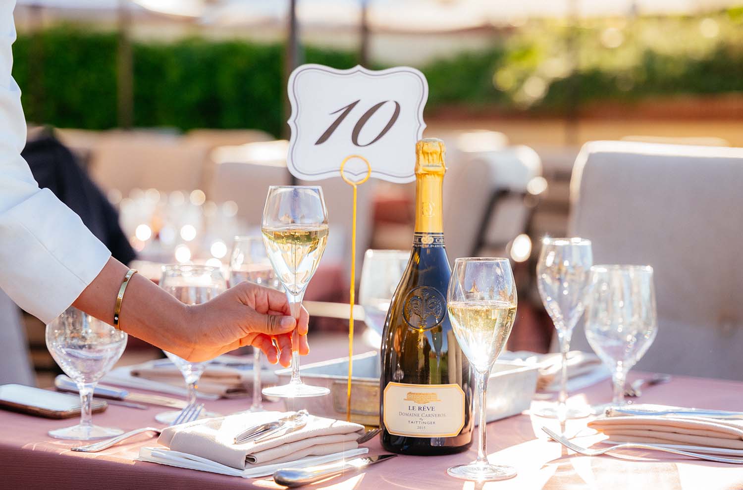 event table setting with hand grabbing sparkling wine flute and wine bottle