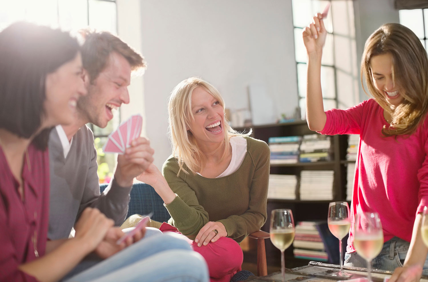 Four people holding cards and laughing with glasses of white wine