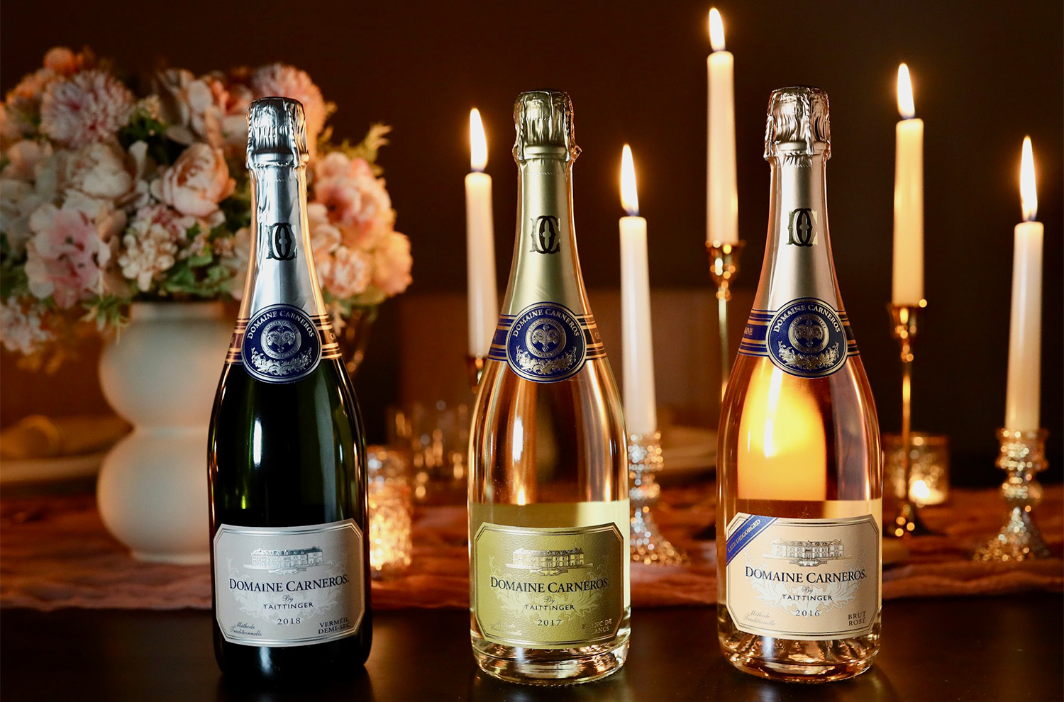 Three bottles of Domaine Carneros wines on dinner table with candles