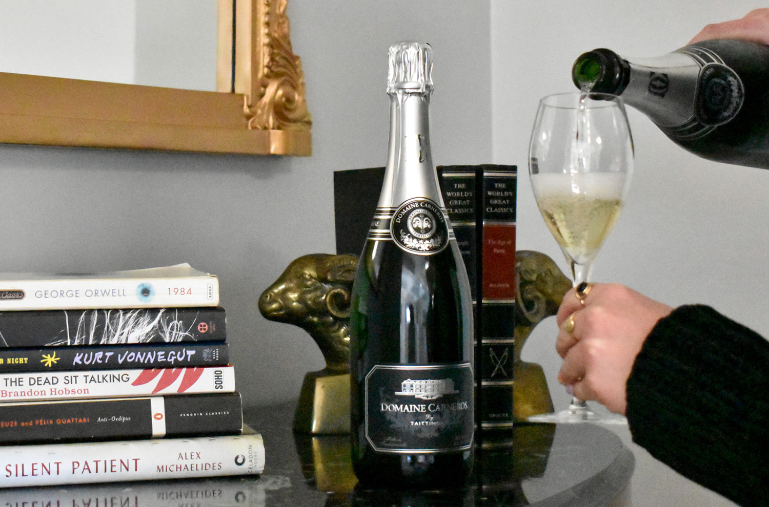 Bottle of Domaine Carneros pouring into glass with stack of books